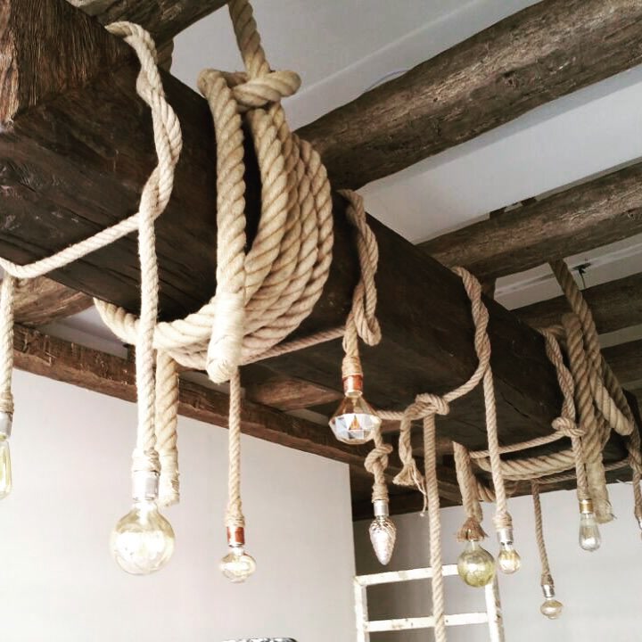 Ahşap kabuğu dokusuna sahip poliüretan kirişler, kalın keten halatlar ve vintage sarkıt lambalarla tamamlanan açık renkli tavan uygulaması.