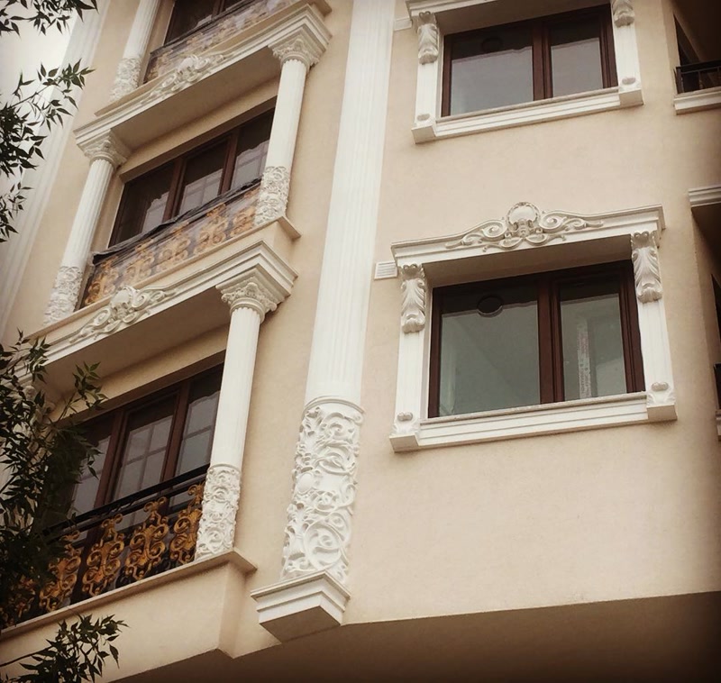 Açık renk bina dış cephesinde uygulanan poliüretan kartonpiyer, dikey sütunlar, dekoratif pencereler, söveler ve taç tasarımları.