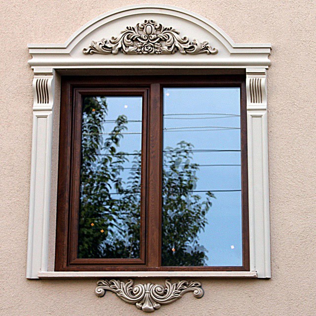 Koyu ahşap pencere doğramasını çevreleyen, açık krem rengine boyanmış kavisli taç ve pilaster sütunlardan oluşan dekoratif pencere çerçevesi.