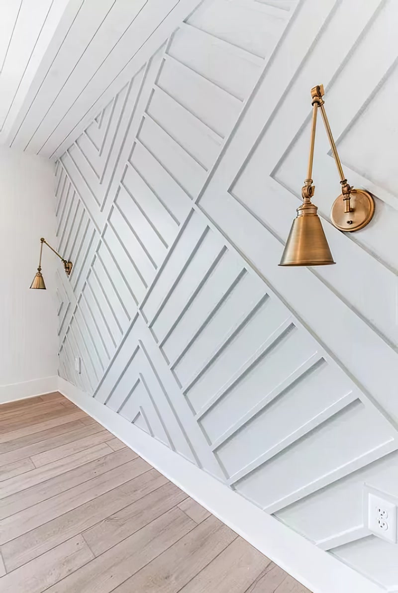 Modern gri tonlarındaki salon duvarında tasarlanmış asimetrik çizgilere sahip duvar profilleri ve yan taraftaki aplik aydınlatmalar.