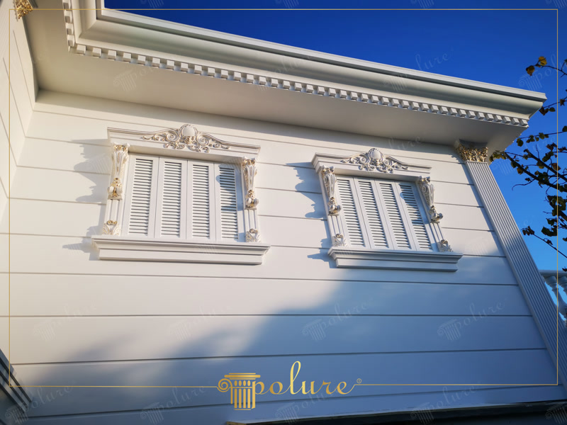 Beyaz poliüretan pencere söveleri, fugalı dış cephe panelleri ve yaldızlı sütun başlıkları ile dekore edilmiş klasik villa cephesi.