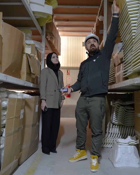 Görevli, farklı profillerin dizildiği üst rafları işaret ediyor.