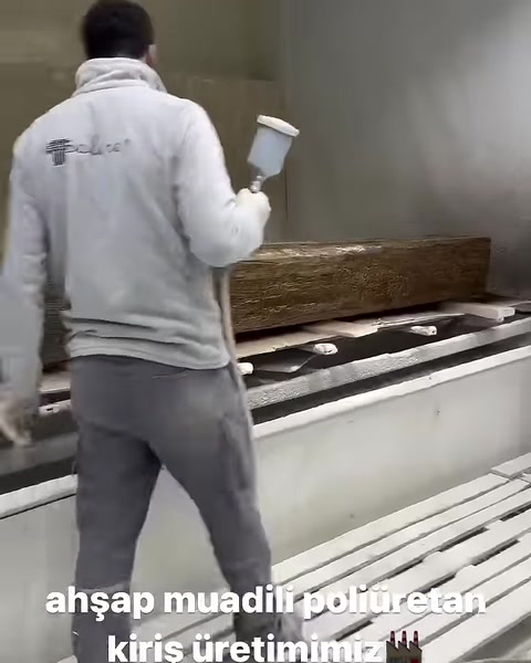 Çalışan ahşap dokulu kiriş yüzeyine tabancayla renk uyguluyor